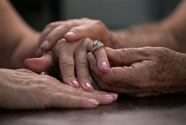 Nyugdíjas pár kezei összefonodva közelről gyűrűvel