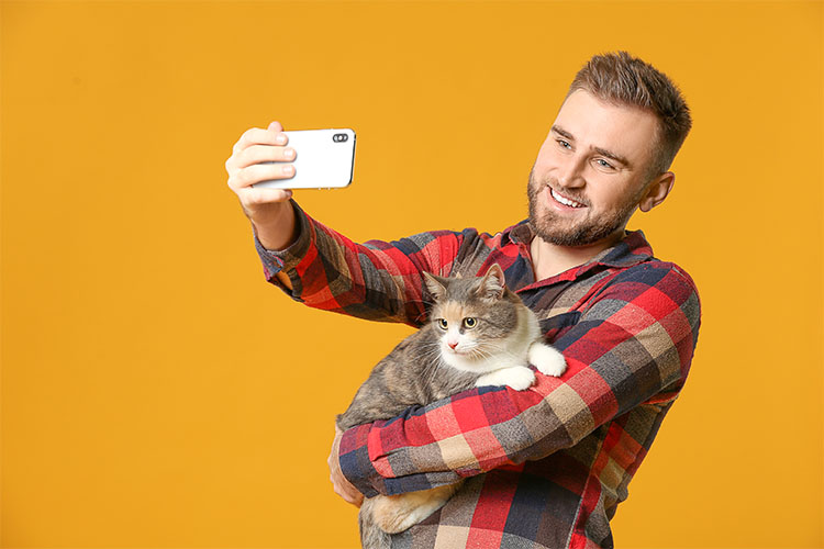 Mosolygós férfi szelfi macskával a karban, sárga háttérrel