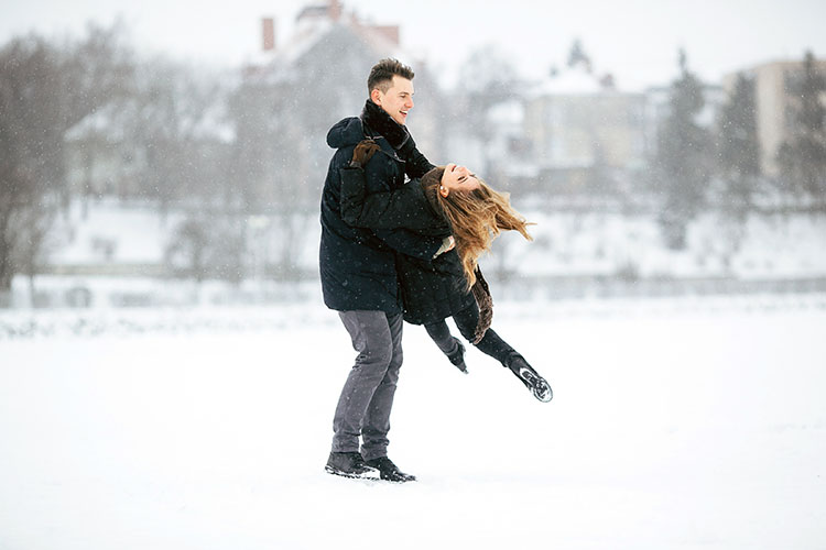 Egy fiatal pár vidáman korcsolyázik a téli jégen, nevetnek és egymás kezét fogják