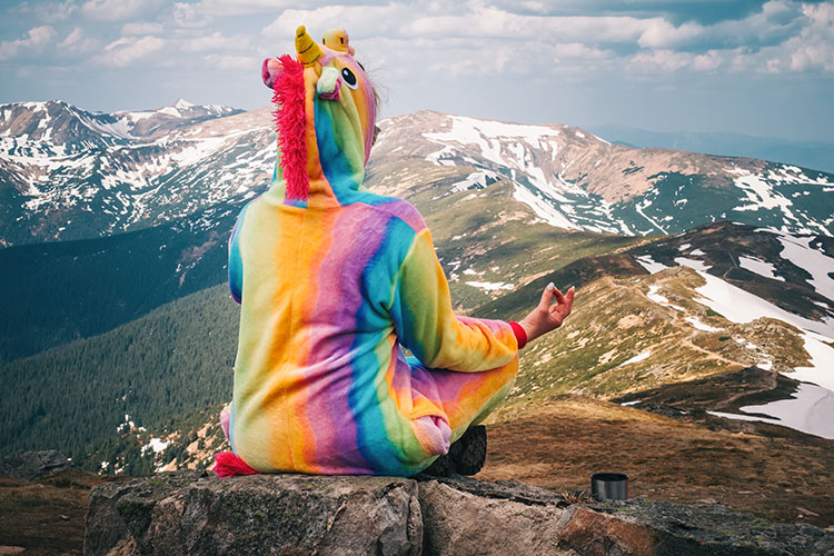 Szivárványos unikornis jelmezben meditáló ember a hegyek között, a túl szépnek tűnő online társkereső helyzetek jelképeként